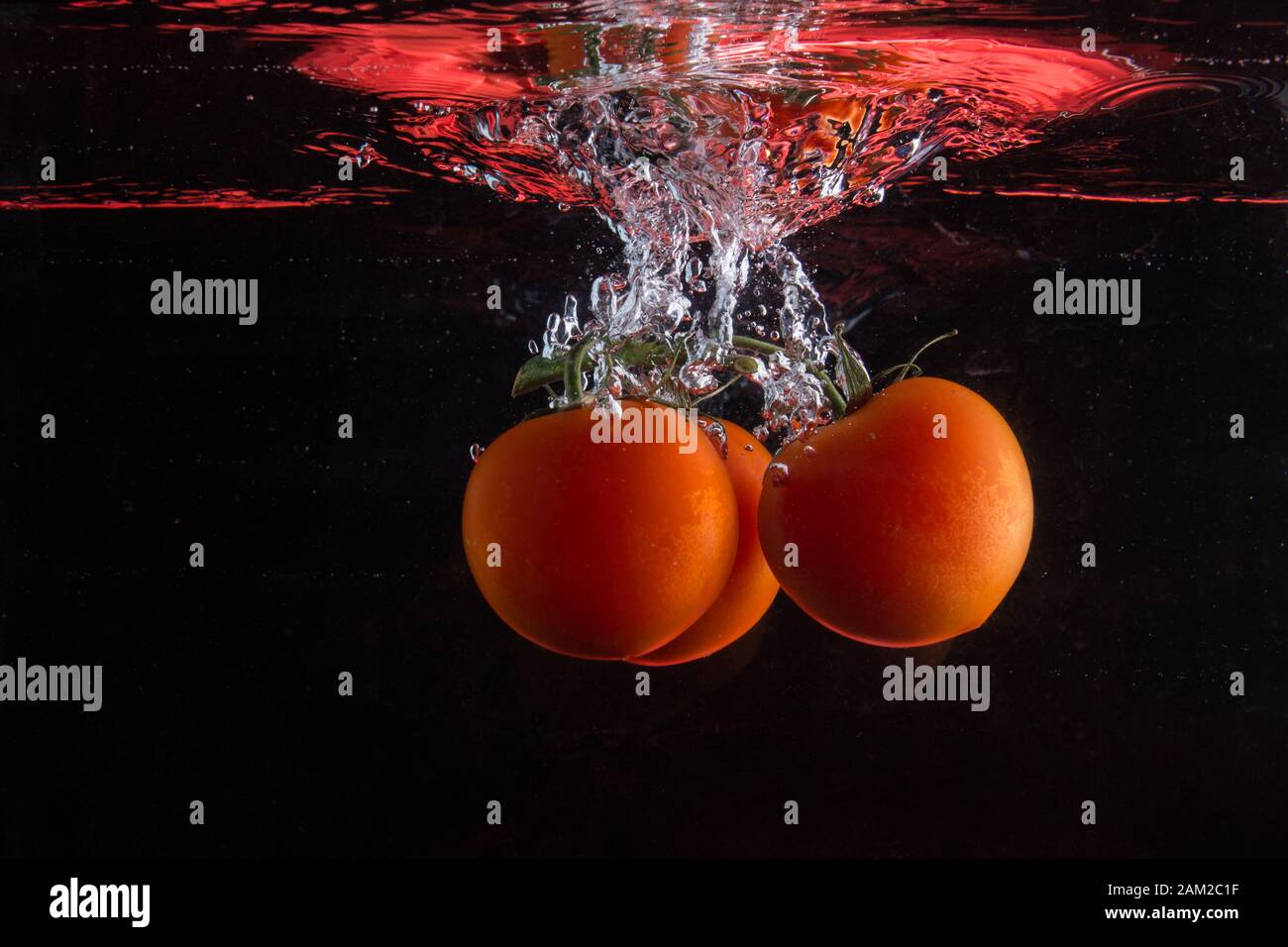 Tomatos falling in water with splash on black background Stock Photo