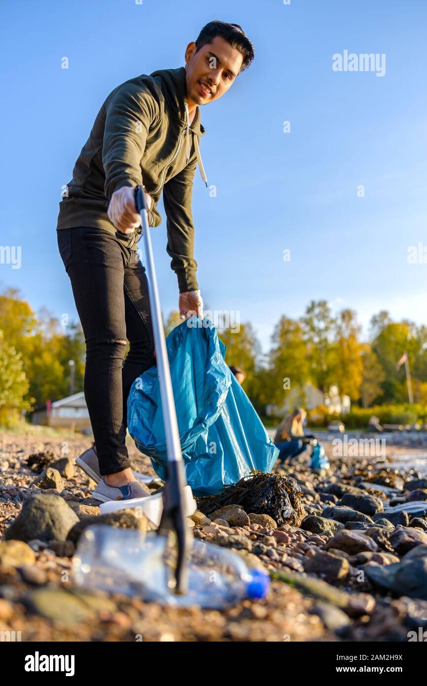 Volunteer picking up garbage with grabber at beach Stock Photo