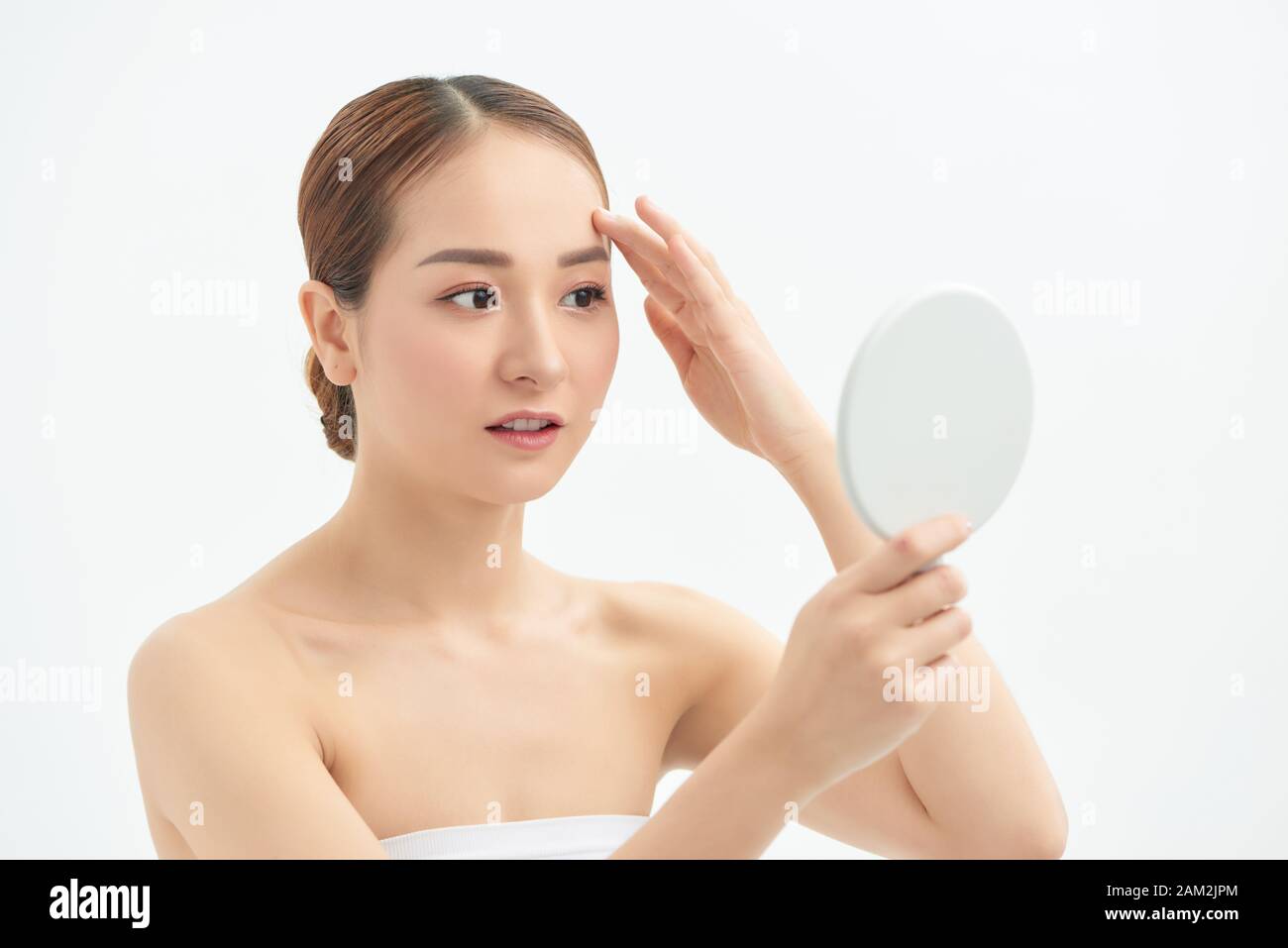 Portrait of young woman with acne problem looking in mirror on white background Stock Photo