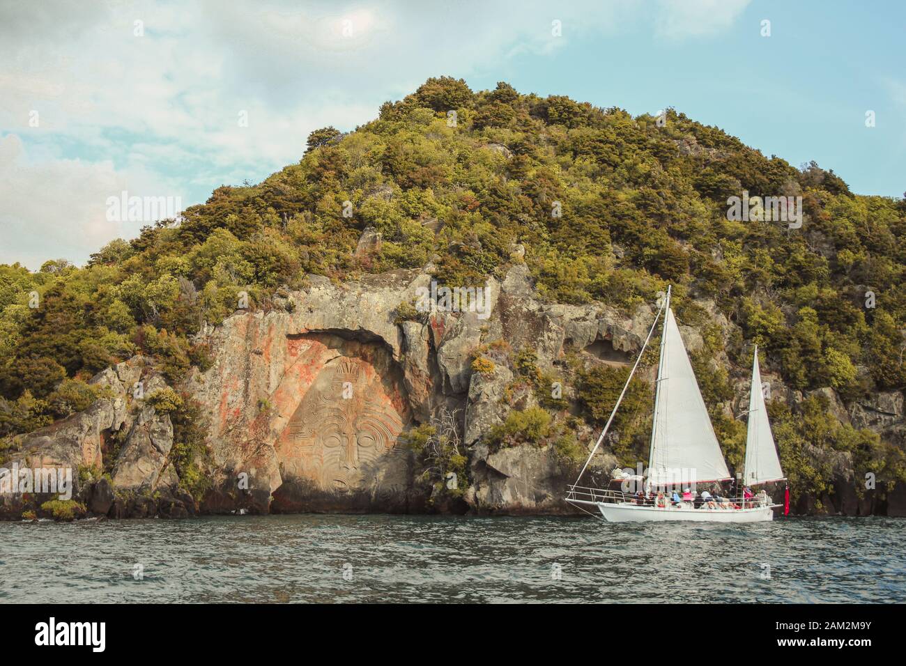 Taupo, North Island, New Zealand - December 26th 2016: Tourists approaching the famous Mine Bay Maori Rock Carvings on Lake Taupo by cruise boat Stock Photo