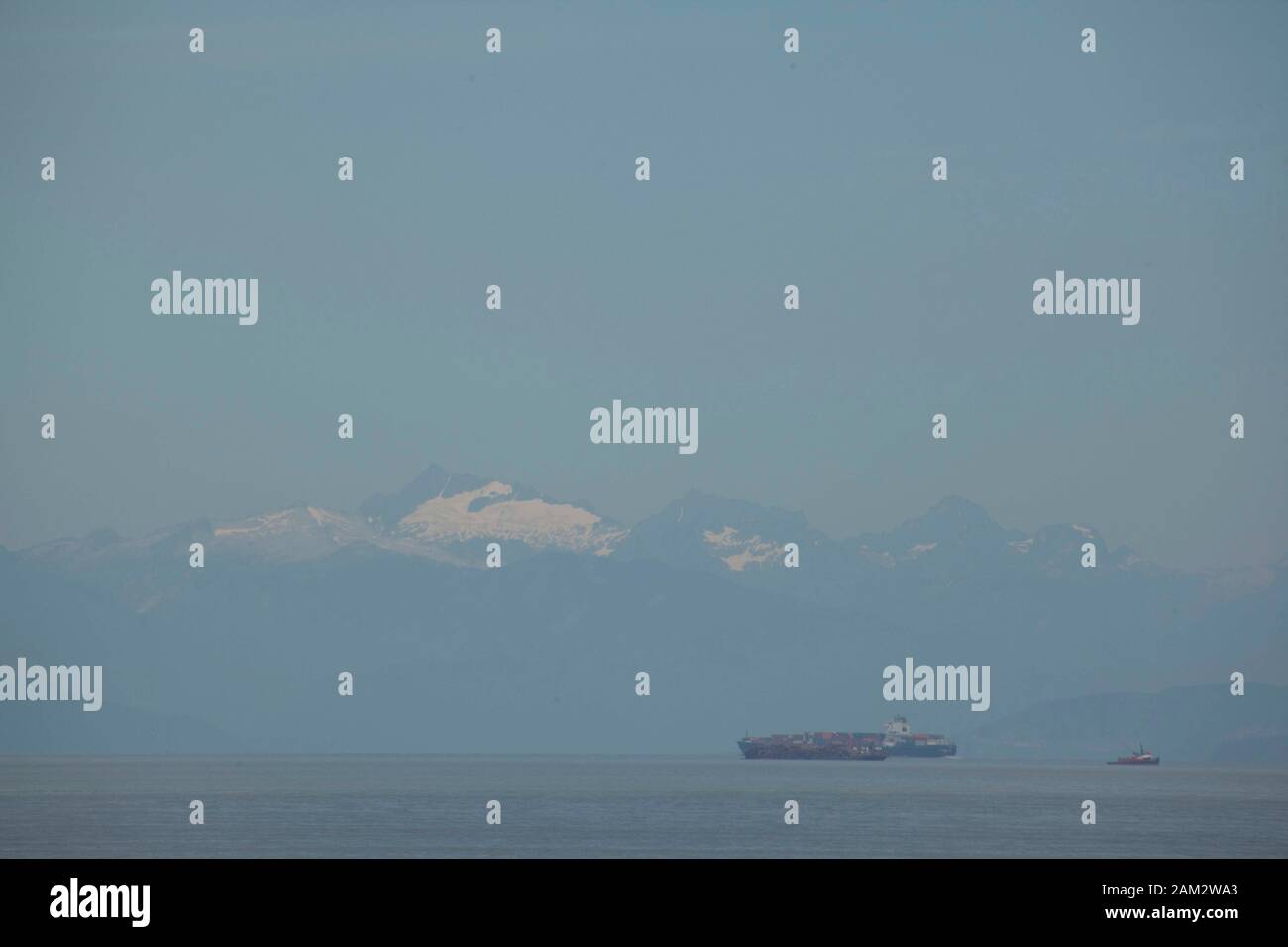 Container ships following tugboat, mountain range in background, Vancouver Island, British Columbia, Canada Stock Photo