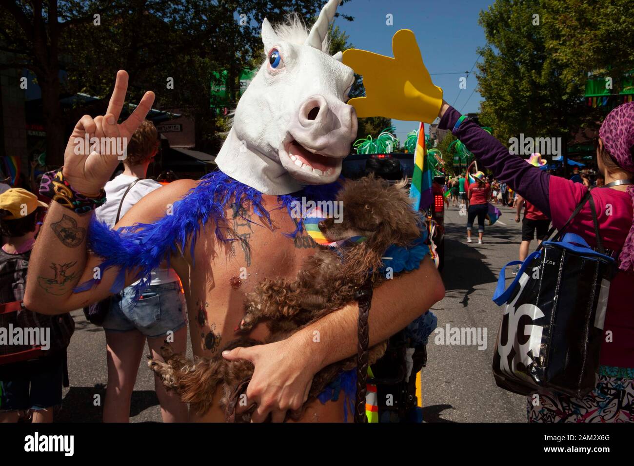 Pride parade participant wearing unicorn head mask making peace sign and carrying pet poodle, Vancouver Pride Festival 2014, Vancouver, Canada Stock Photo