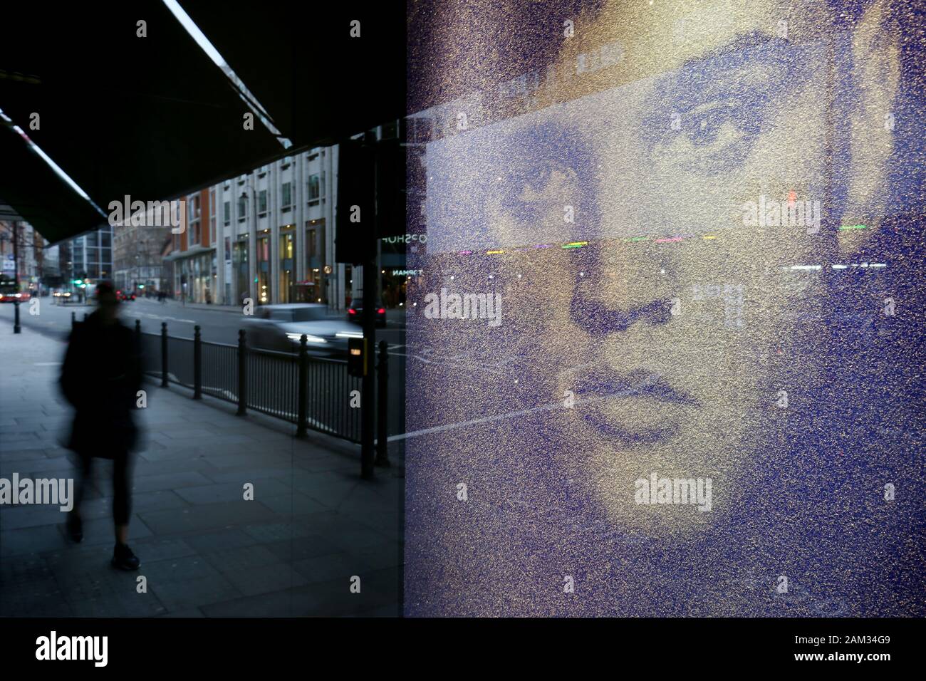 Pedestrians and traffic are reflected in a shop window display of a diamond dust portrait of Elvis Presley by Russell Young on the Knightsbridge storefront of Harrods, London. Stock Photo