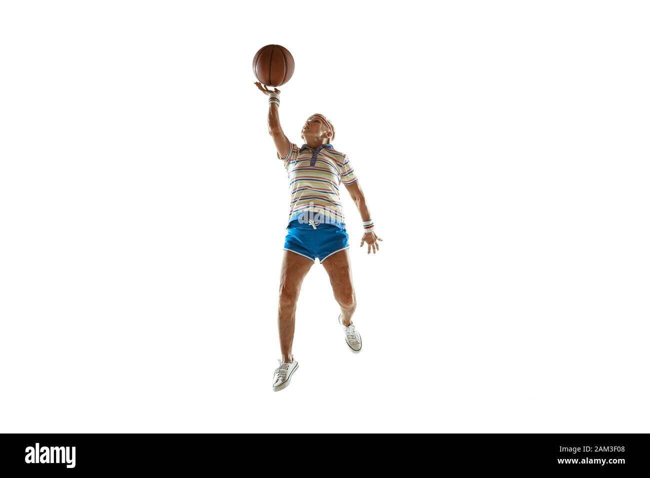 Move. Senior woman wearing sportwear playing basketball on white background. Caucasian female