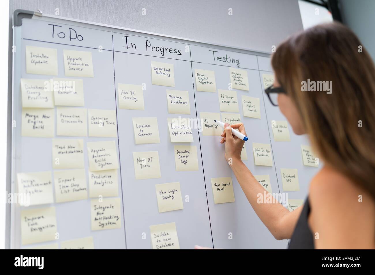 Side View Of Businesswoman Writing On Sticky Notes Attached To White Board In Office Stock Photo