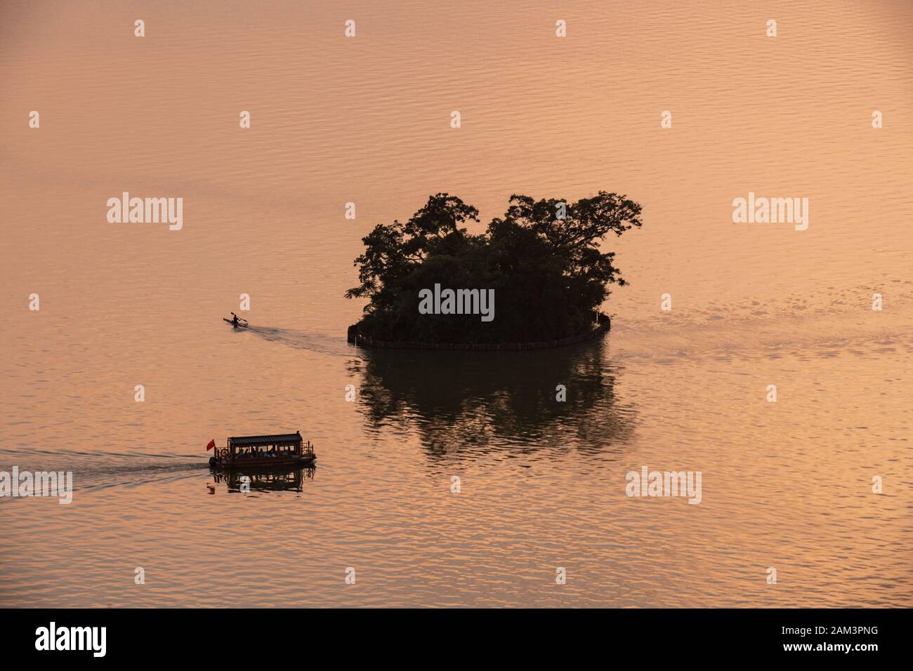 A boat and a lone canoeist paddle towards an island at sunset in the Seven Star Crags national park, near zhaoqing, People's Republic of China Stock Photo