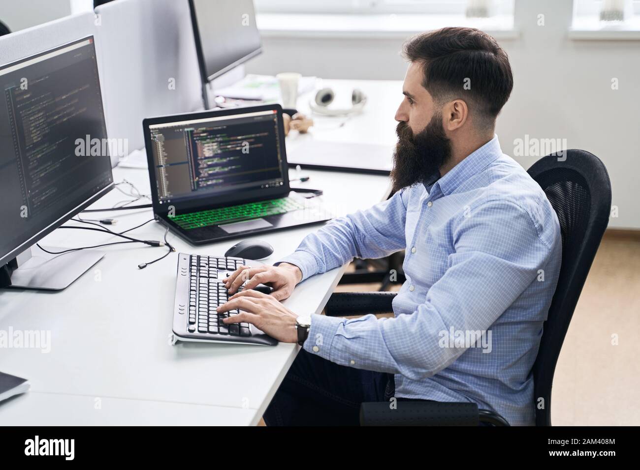 Computer programmer developer working in IT office, sitting at desk and coding, working on a project in software development company or startup. Stock Photo