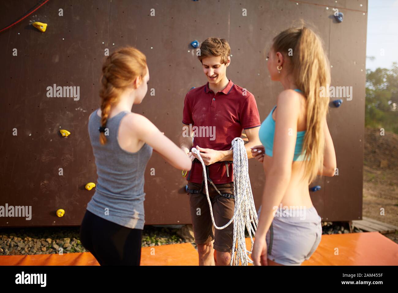 Rock climbing instructor is coaching how to tie knot. Male coach fixing