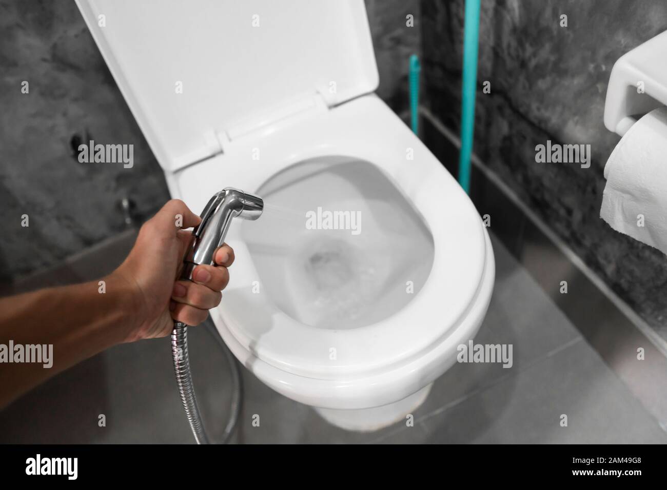 Using of bidet shower with a white toilet. Bidet shower in male hand for  using with a white toilet bowl Stock Photo - Alamy