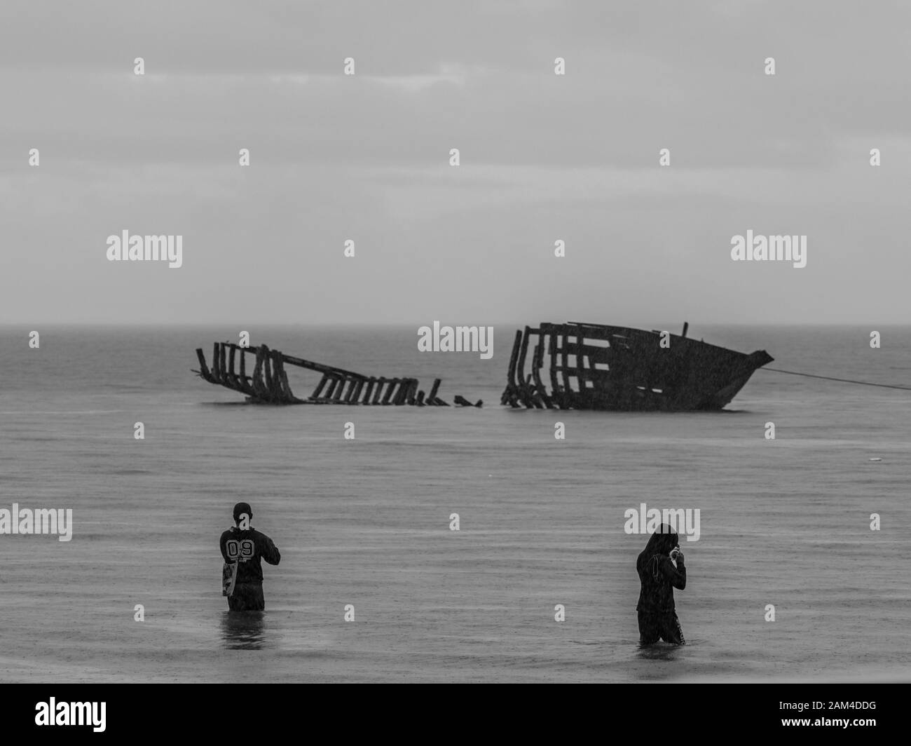 View of the silhouettes of a destroyed boat and a fishermen during high tide on the Saram Sea. Rainy weather.  Kaimana, Bird's Head Peninsula, West Pa Stock Photo