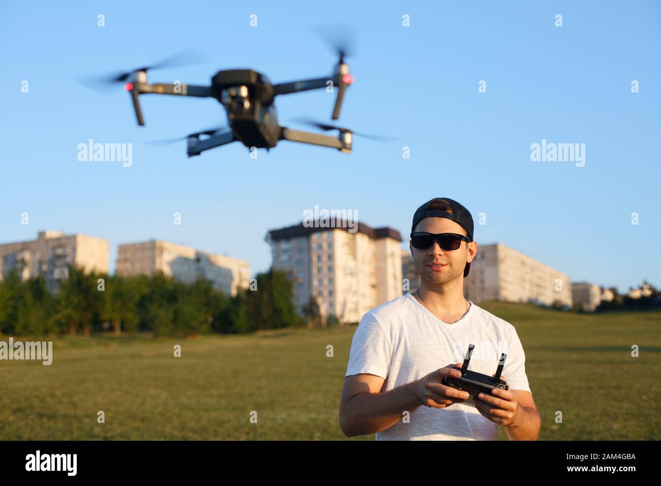 Compact drone hovers in front of man with remote controller in his hands. Quadcopter flies near pilot. Guy taking aerial photos and videos from above Stock Photo