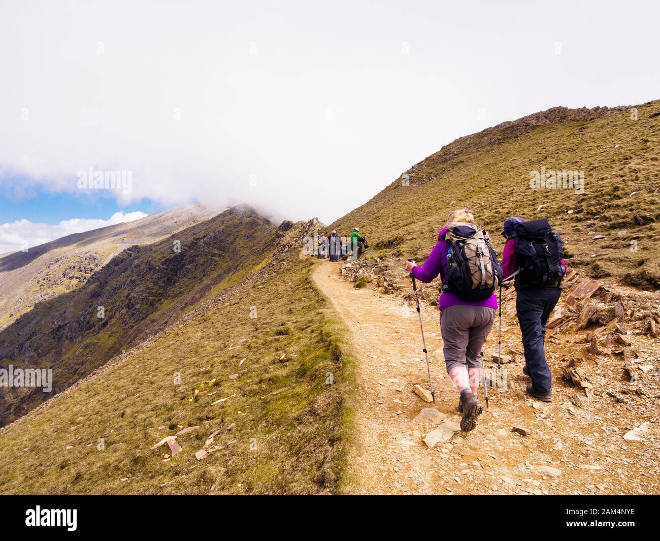 Hikers hiking on Rhyd Ddu path on Bwlch Main with view to low cloud on Mt Snowdon summit in Snowdonia National Park, Gwynedd, North Wales, UK, Britain Stock Photo