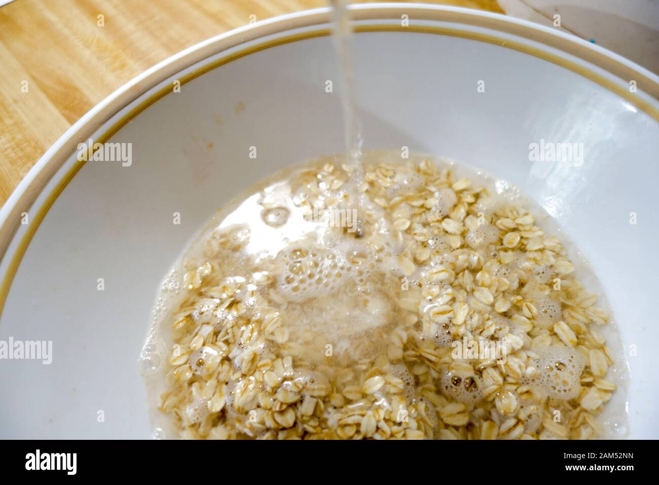 Breakfast Oatmeal in white bowl, Water being poured on dry rolled