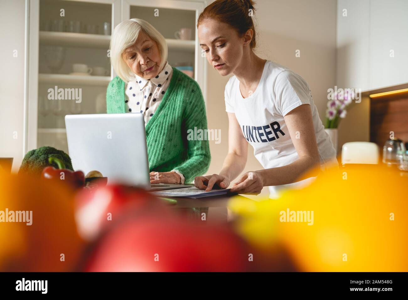 Two females leaning on table while using laptop Stock Photo
