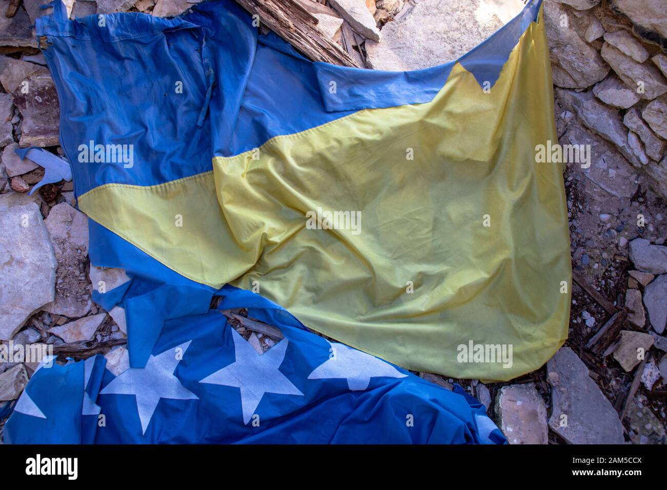 Torn flag of Bosnia and Herzegovina on the ground. Lost in the rubble. Representation of division of serbian,croatian and muslim nations. War in Bosni Stock Photo