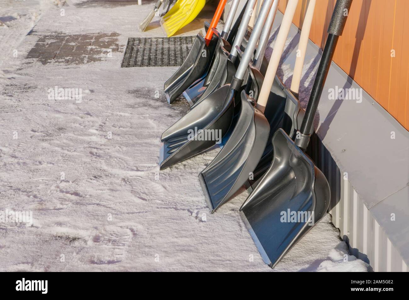 Snow shovels ready for use stand along a wall outside on a Sunny winter  day. Copy space Stock Photo - Alamy