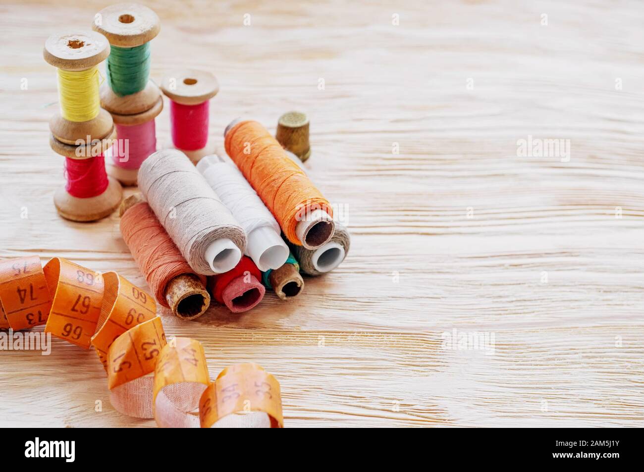 Close-up of various colored spools of sewing thread lie on a wooden table. Copy space. Stock Photo