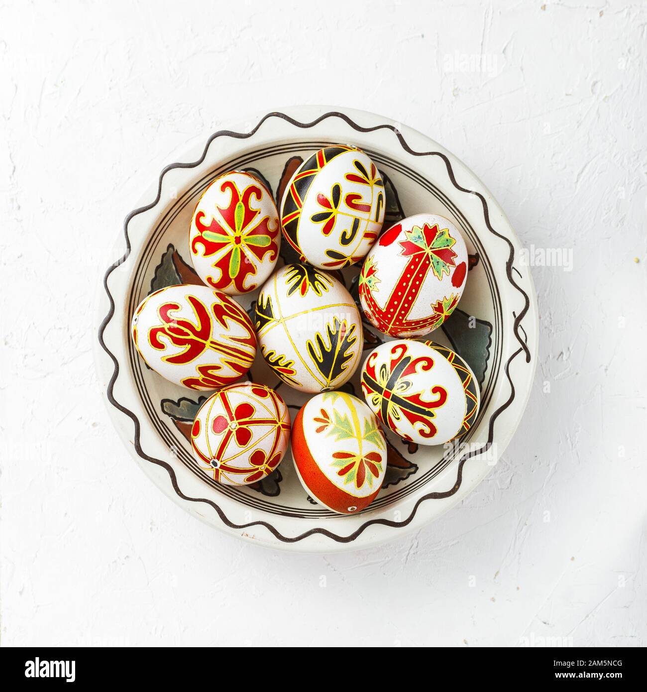 Ukrainian Easter eggs decorated with wax-resist dyeing technique. Pysanky in a bowl, top view, white background Stock Photo