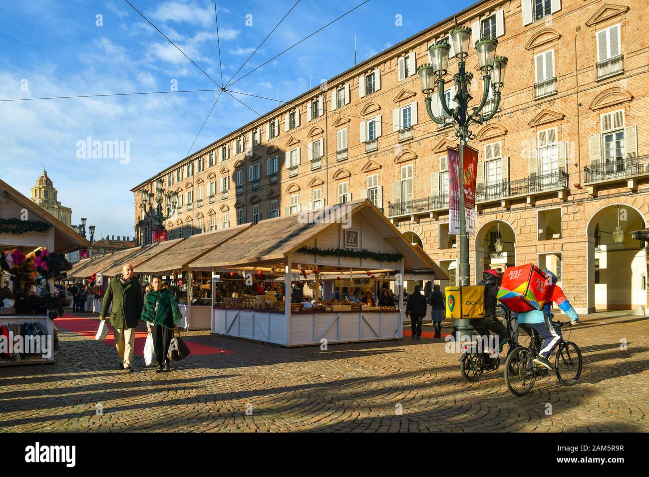 Traditional Christmas market in Piazza Castello square with people shopping and two bike delivery guys of Glovo and Just Eat, Turin, Piedmont, Italy Stock Photo