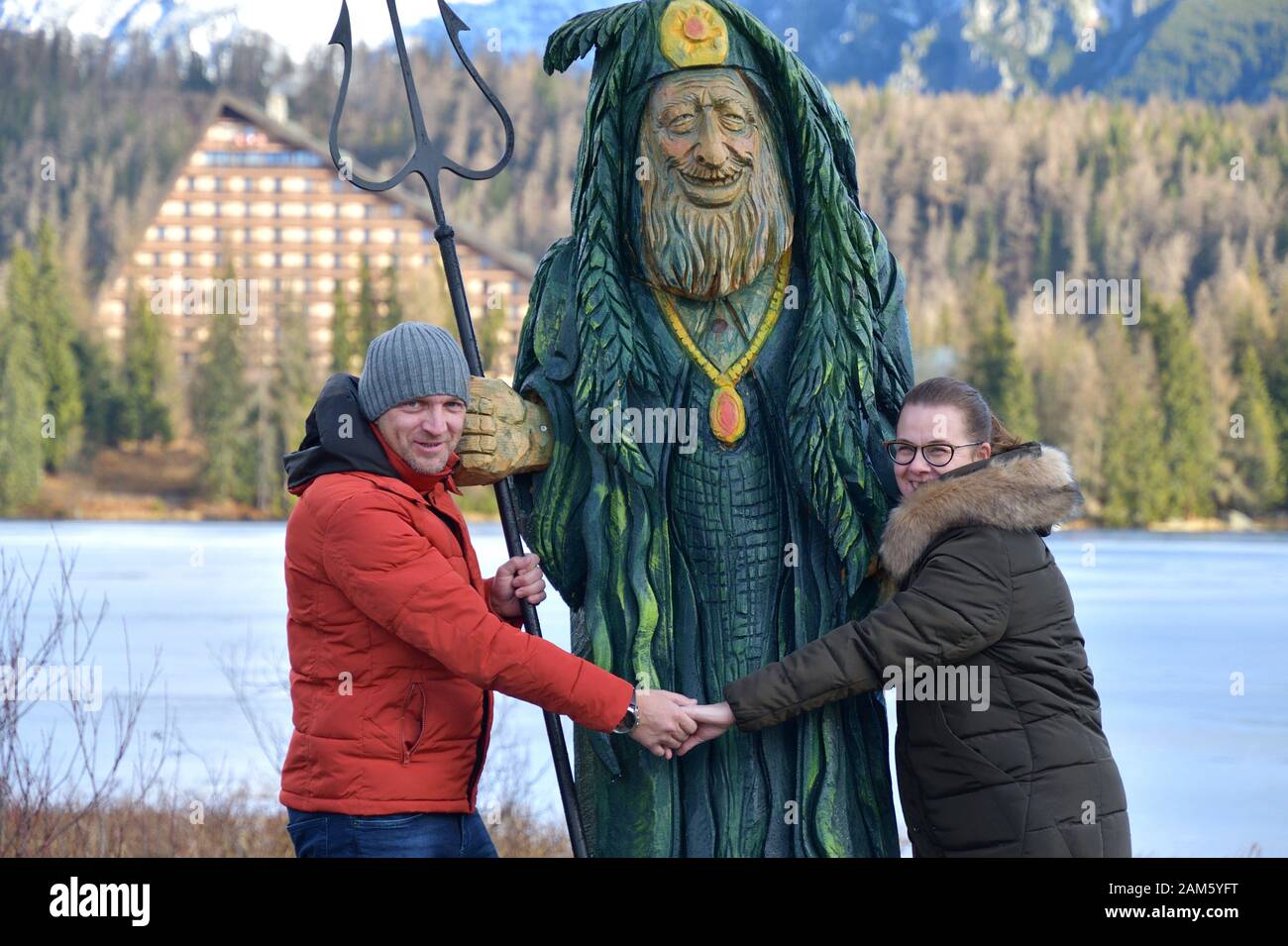 Woman and man fallen in love holding hands in embrace of wooden statue ...