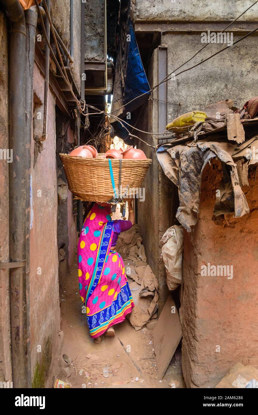 Indian woman carries basket with clay pots on her head on the street in Dharavi Slum at Mumbai. India Stock Photo