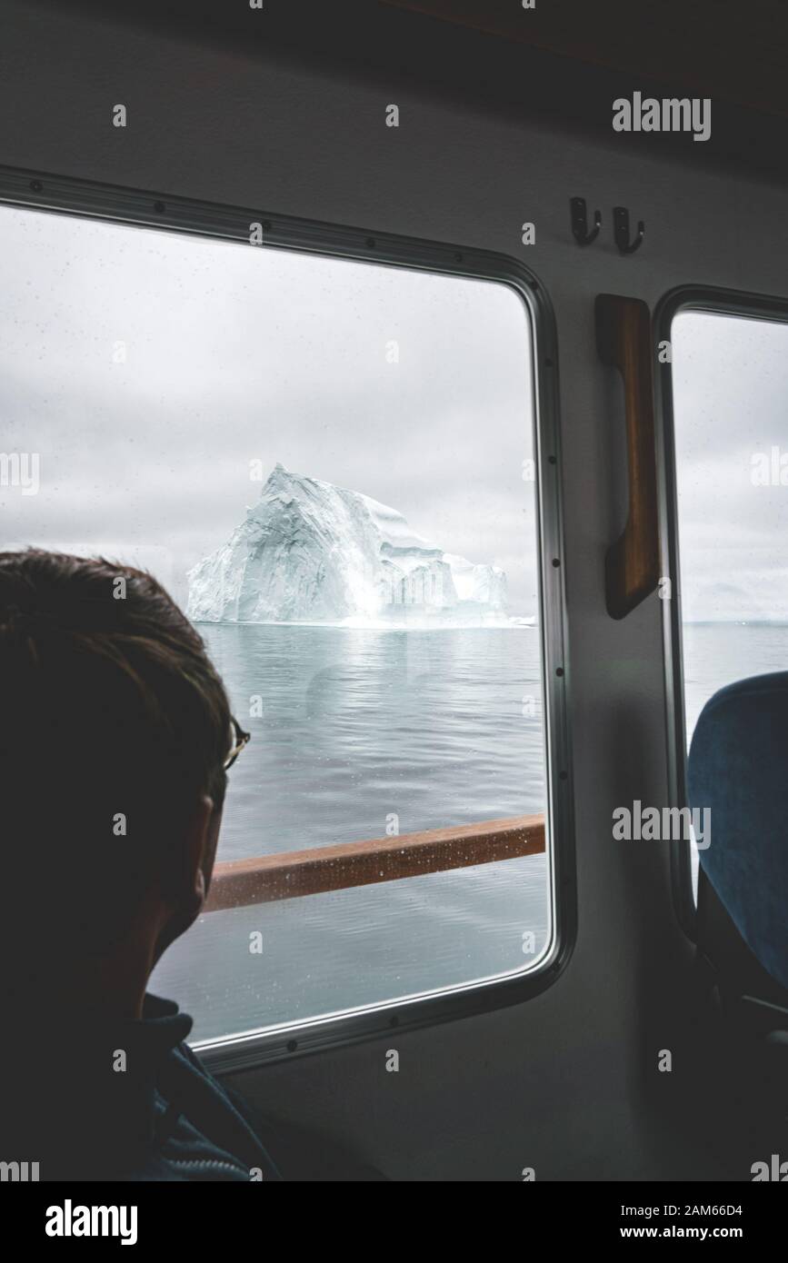 Tourist Looking at Glaciers and icebergs Mountains on a boat in west greenland. Iceberg in sea and ocean. Overcast day. Male traveler. Stock Photo