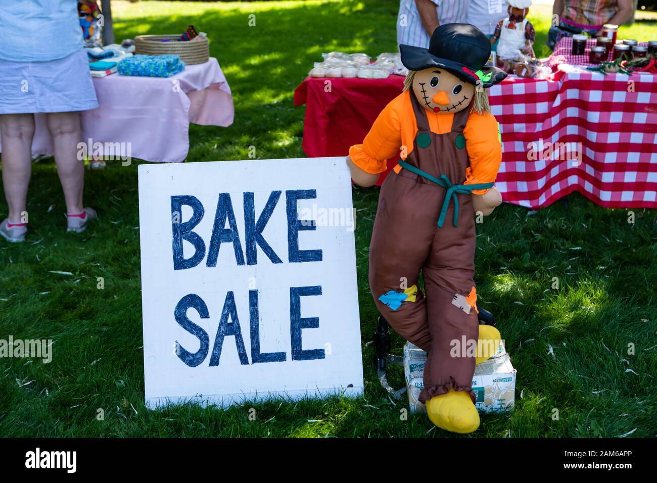 Farmer doll holds Bake Sale sign at outdoors. Different bakery products