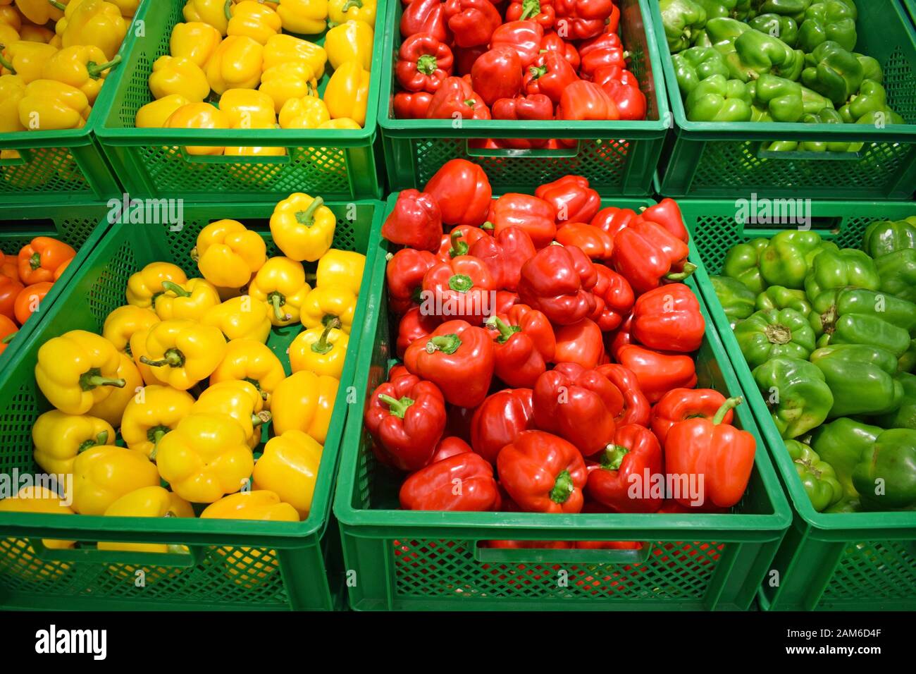 Red, yellow and green peppers in a plastic box on a store counter