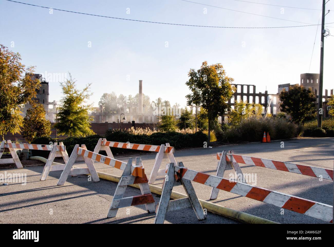 Wooden street barricades are set up to prevent traffic from going to the burning and smoke filled industrial building in the background. Stock Photo