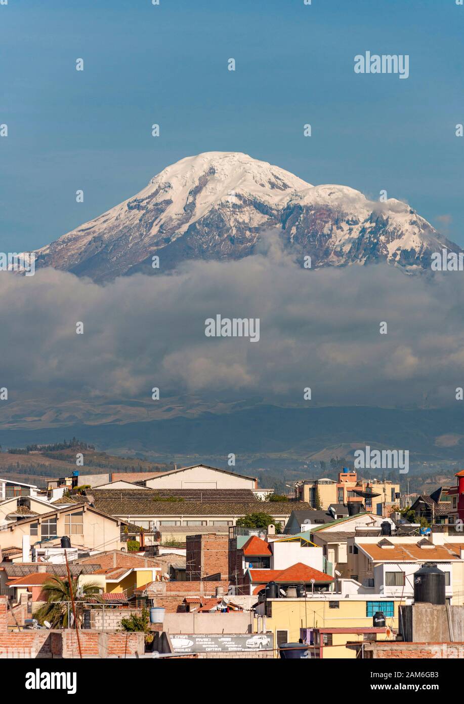 Mount Chimborazo volcano (6268m) seen across the rooftops of the town of Riobamba. Stock Photo