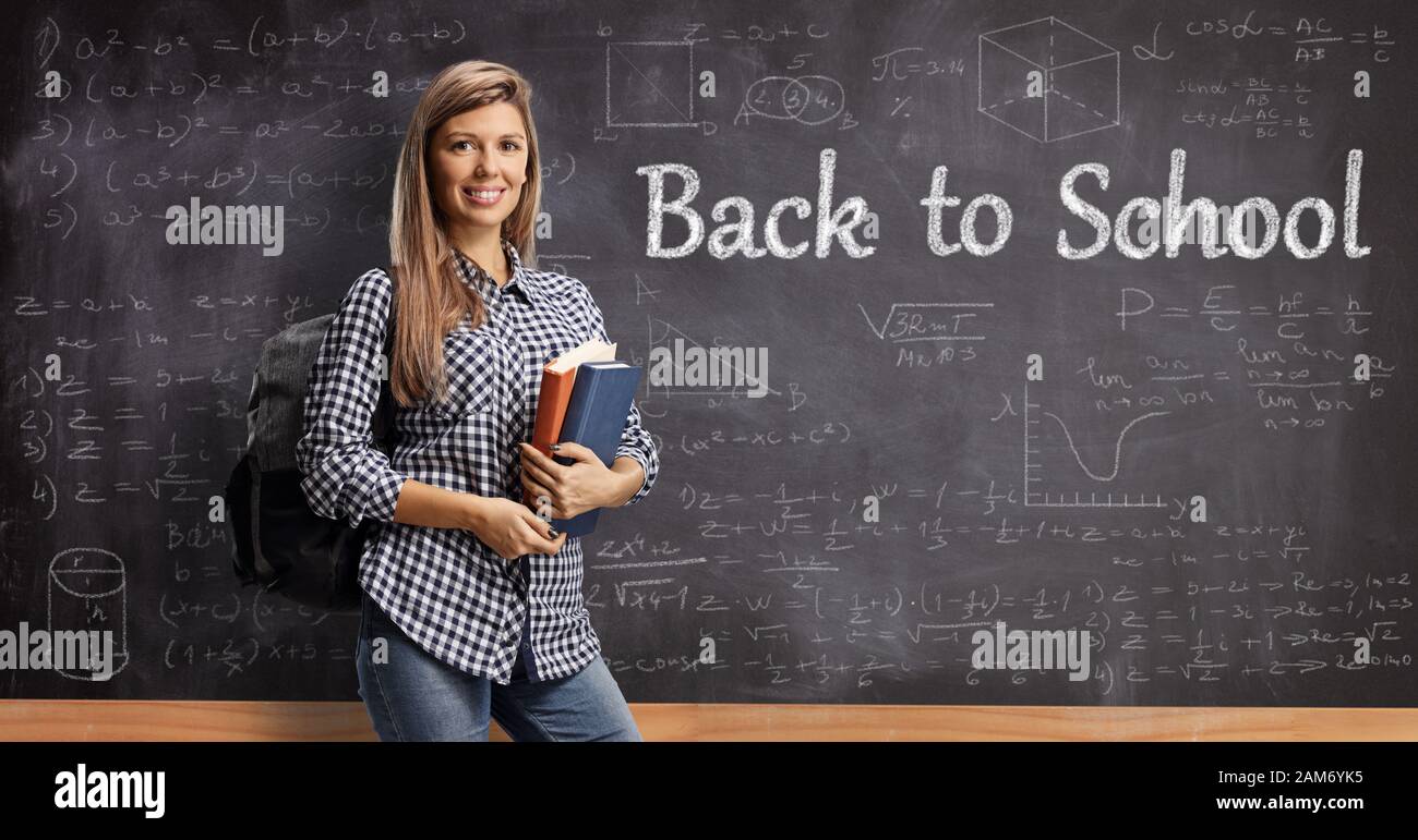 Female student holding books in front of a school blackboard with text back to school Stock Photo