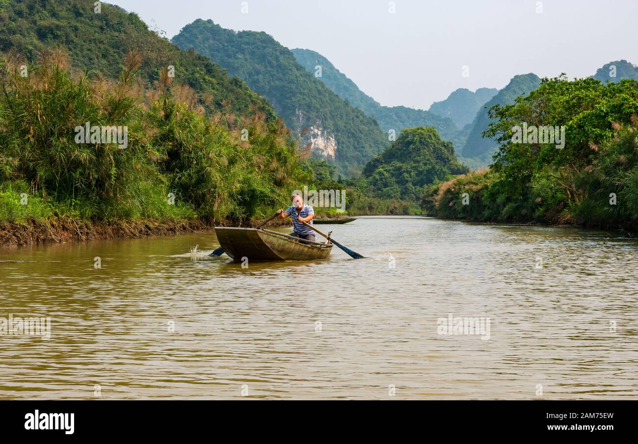 Local Asian man rowing sampan on river with view of limestone karst mountains, Tam Coc, Ninh Binh, Vietnam, Asia Stock Photo