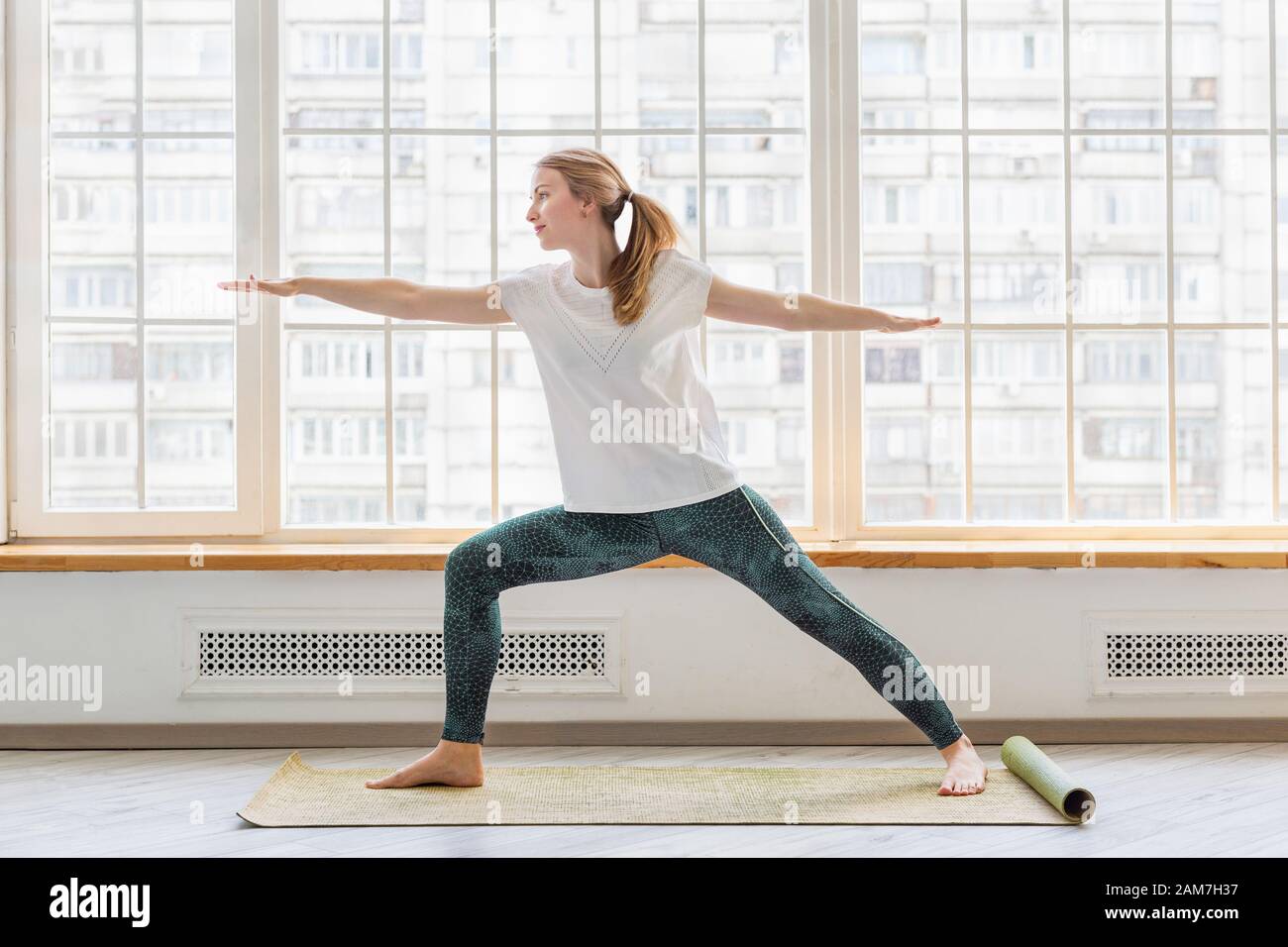Young woman doing yoga on yoga mat in front of window Stock Photo