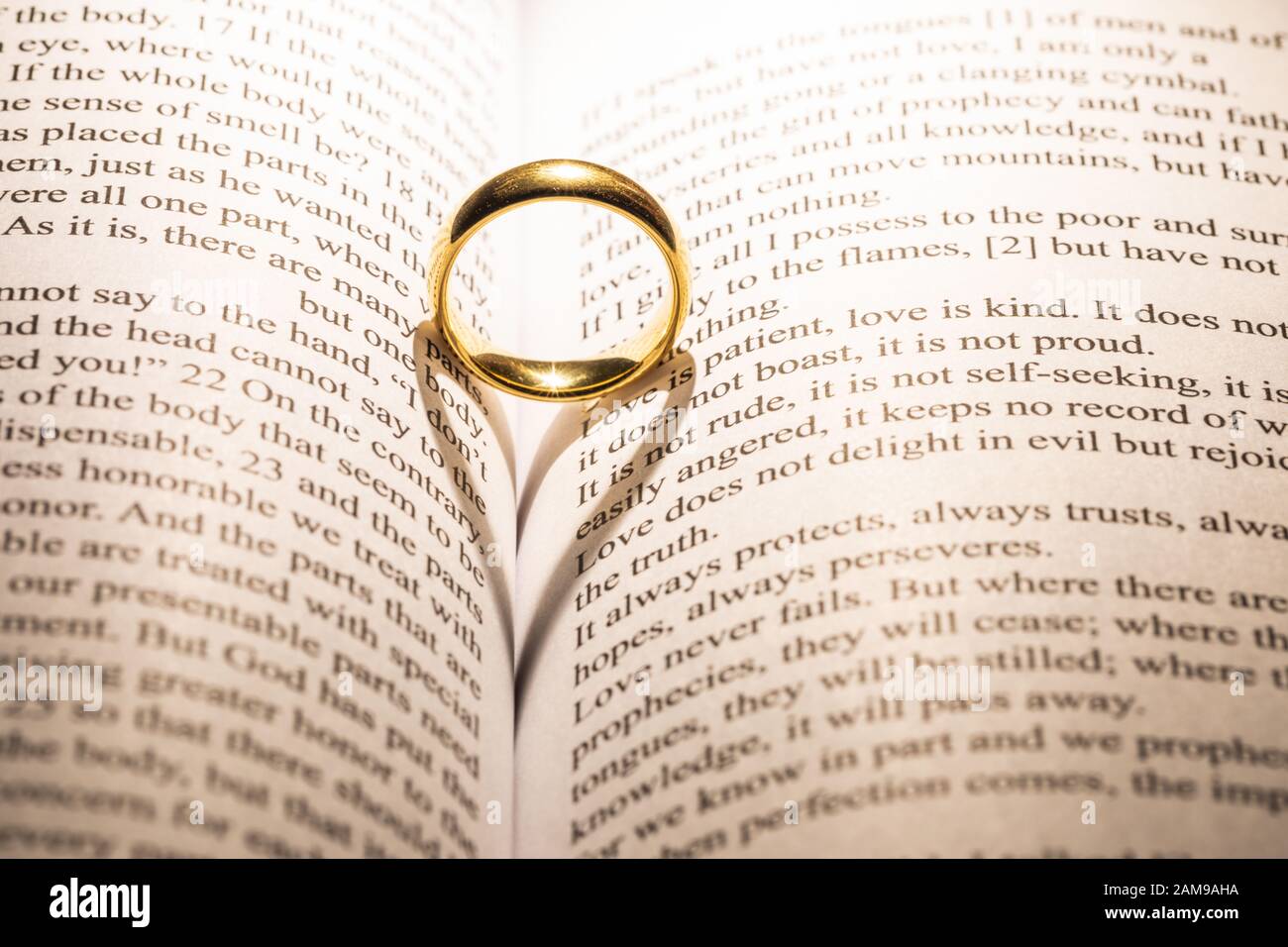 One golden wedding ring on Holy bible book with heart shaped shadow