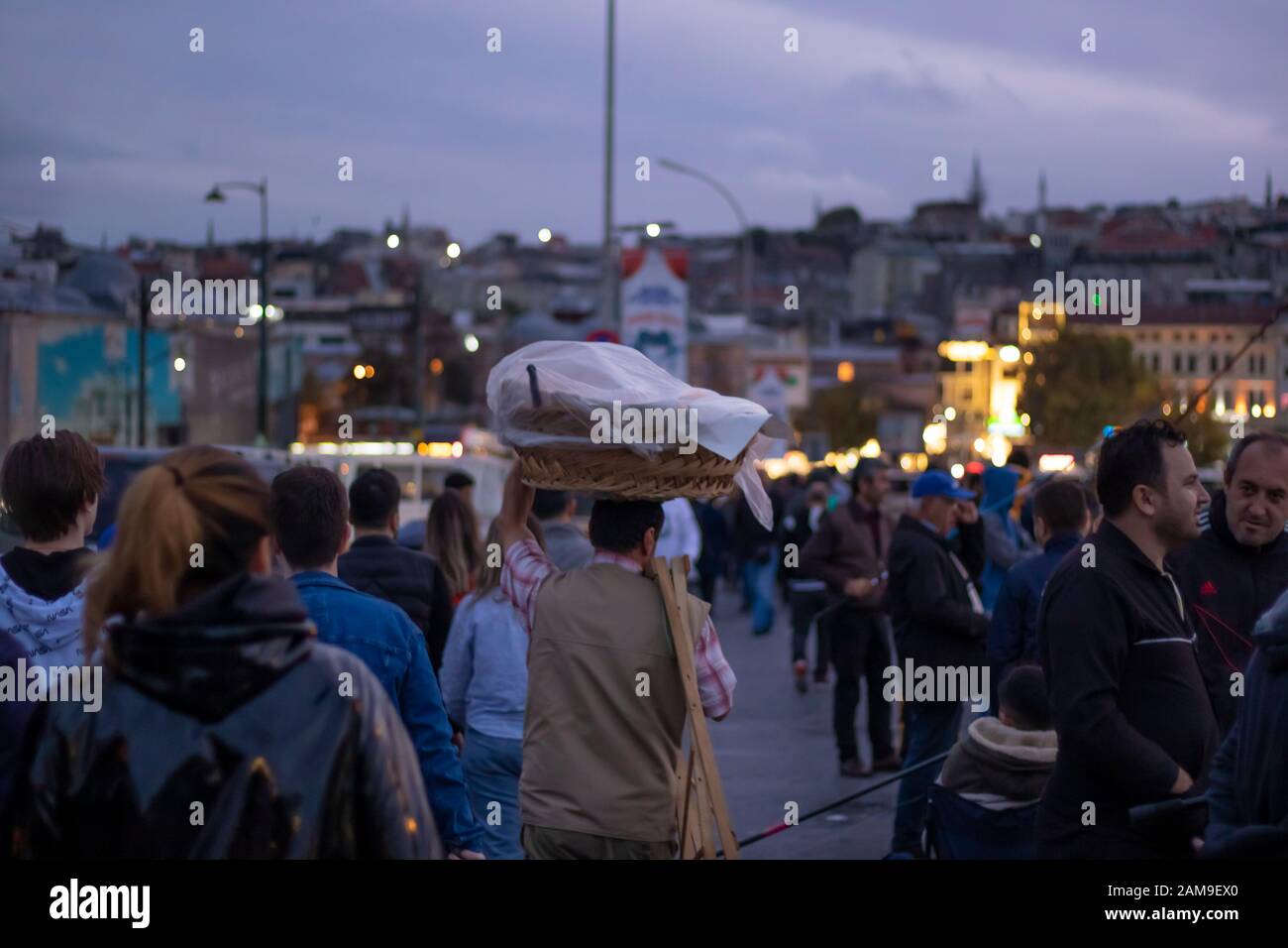 Bagel salesman among people. He carries the bagels on his head. Photographed in the evening. Photographed on the Galata Bridge. Stock Photo