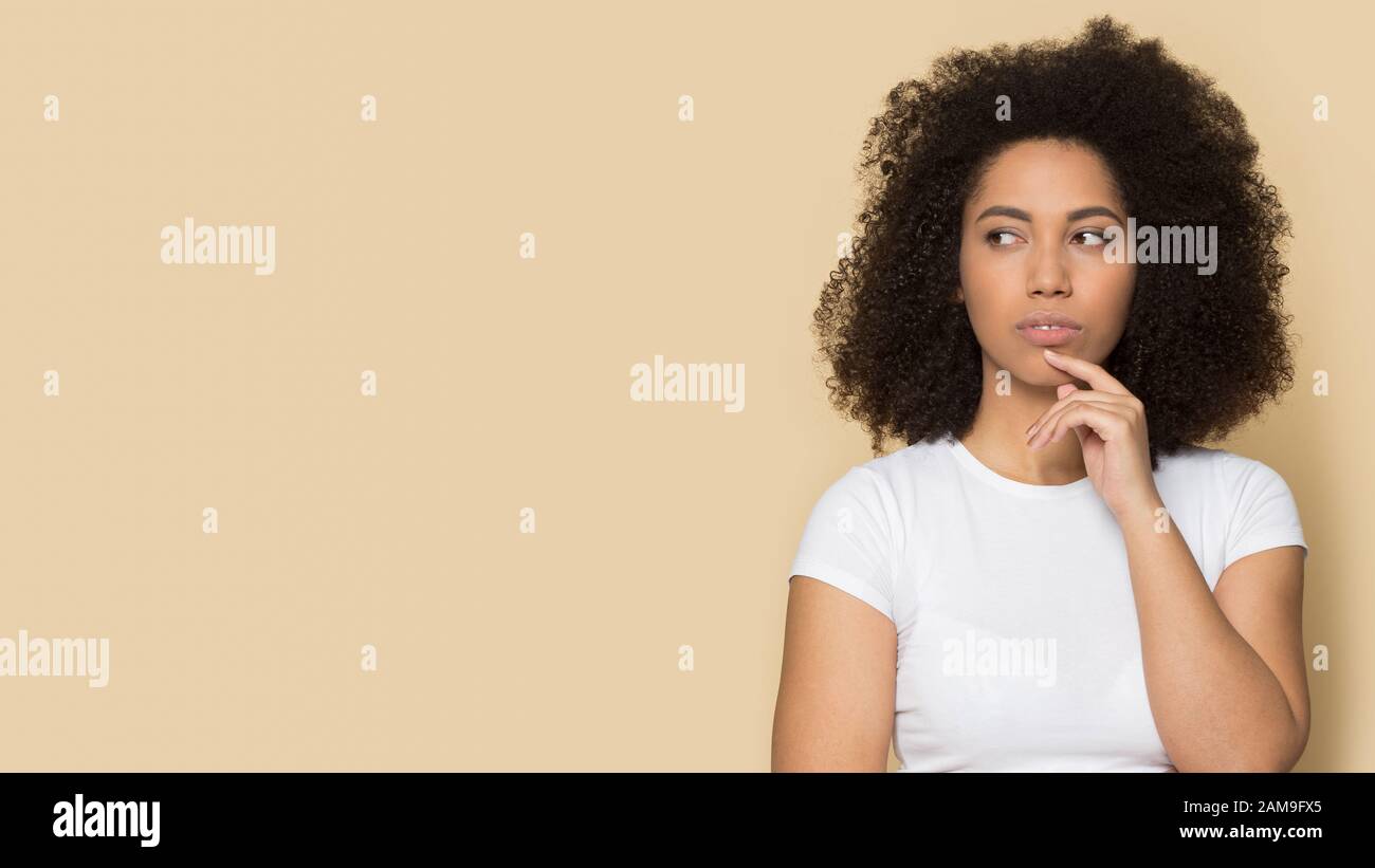 Pensive thoughtful doubtful young african american lady touching chin. Stock Photo
