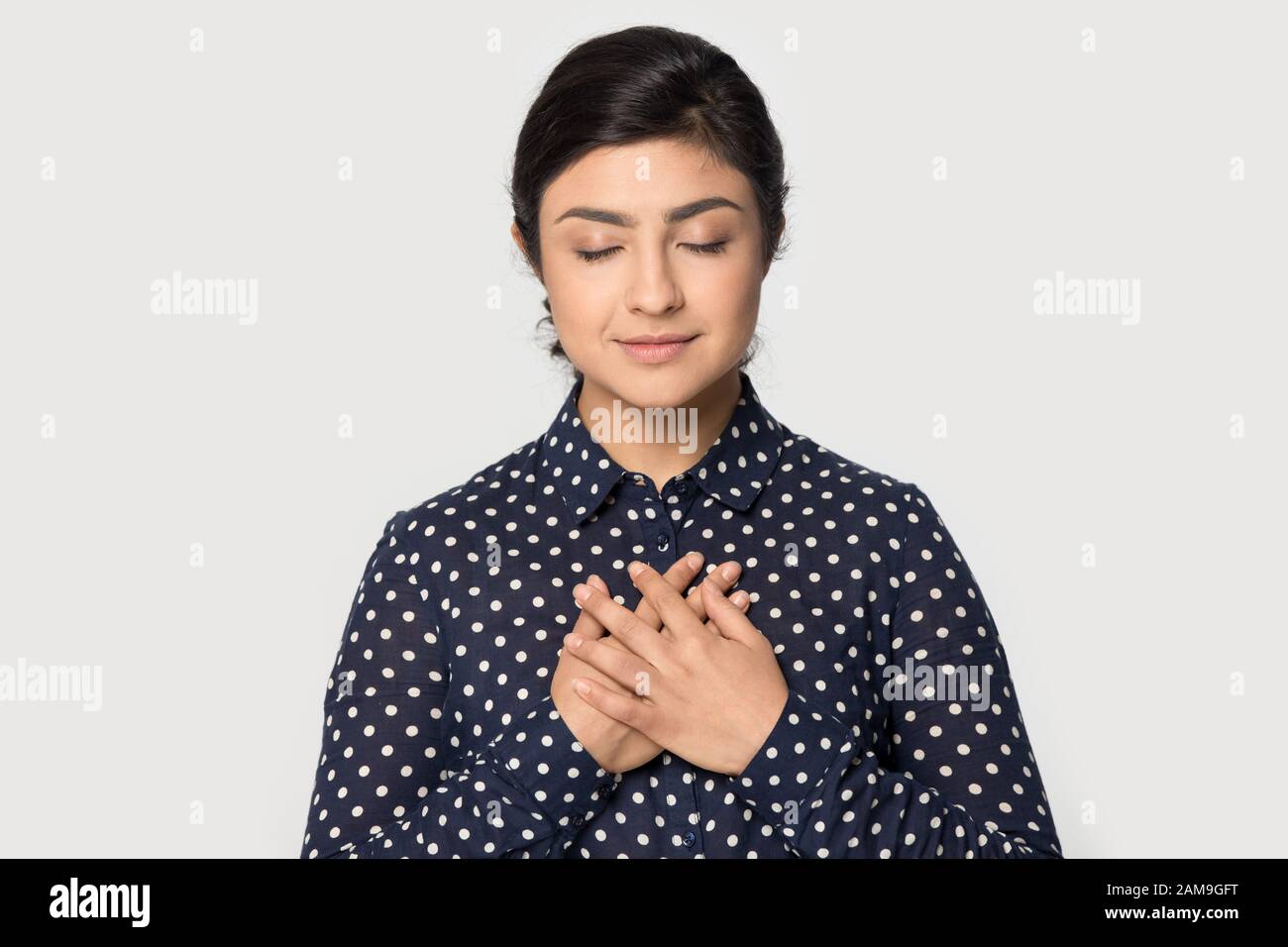 Grateful young attractive indian girl folding hands on chest Stock
