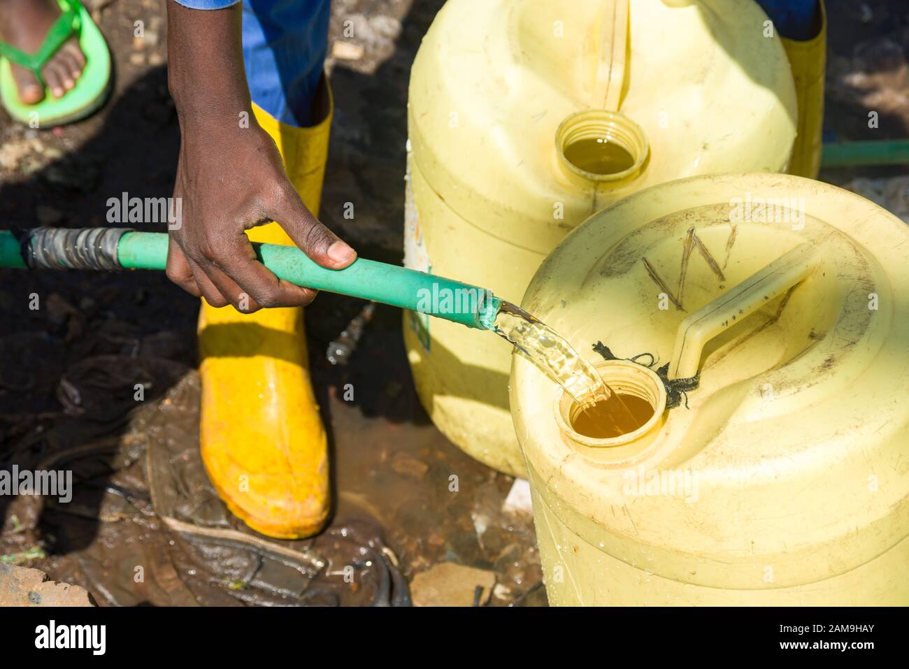 A young man filling yellow water containers from a fresh water pipe, Korogocho slum, Nairobi, Kenya Stock Photo