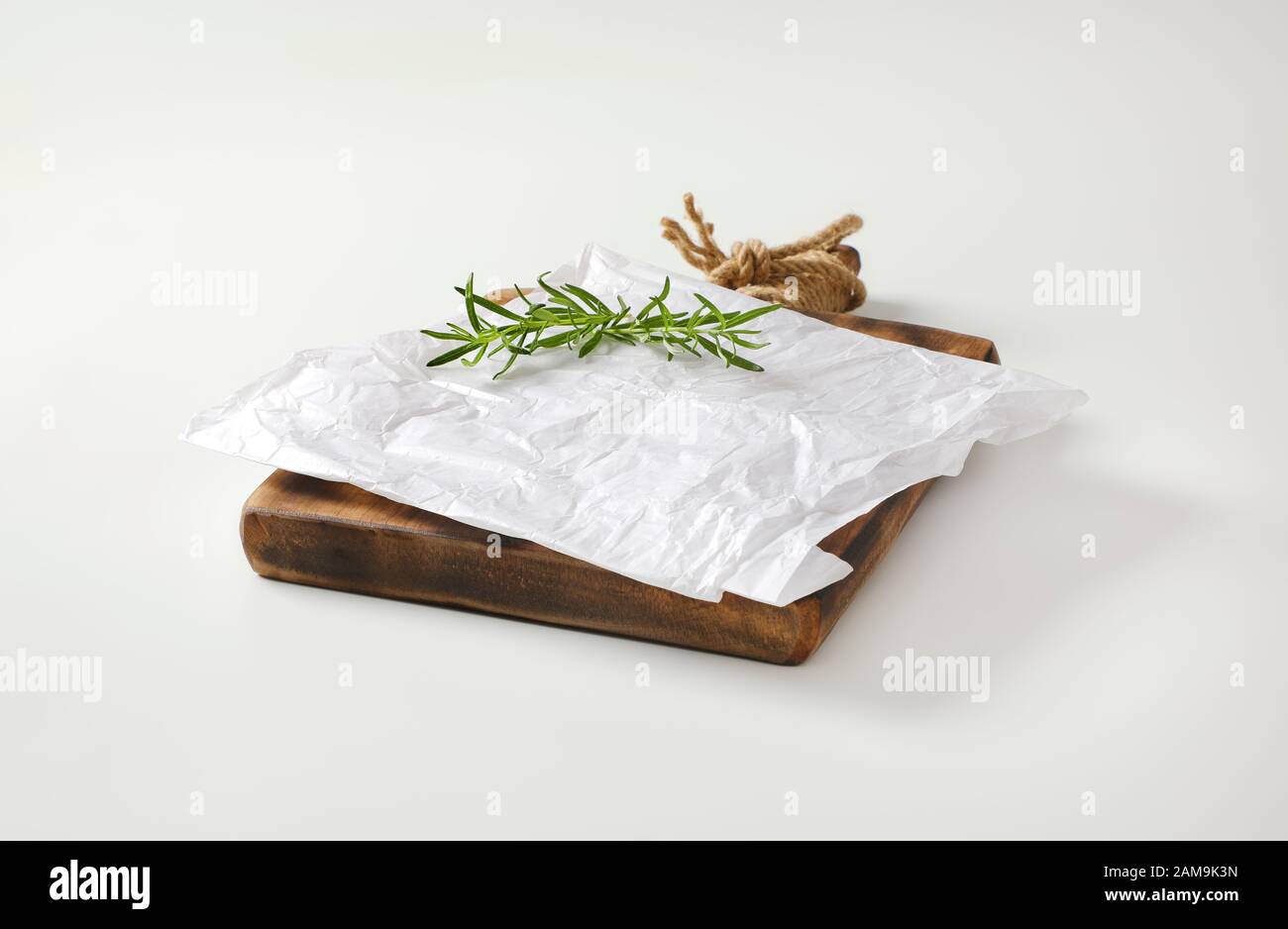 Creased sheet of white wax paper and fresh rosemary on cutting board Stock Photo