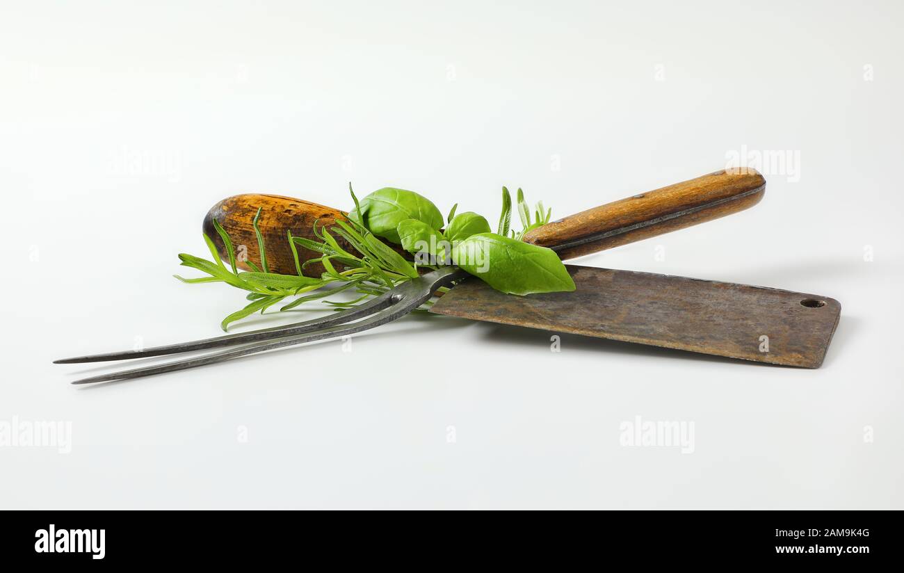 Old meat cleaver knife, carving fork and fresh culinary herbs Stock Photo