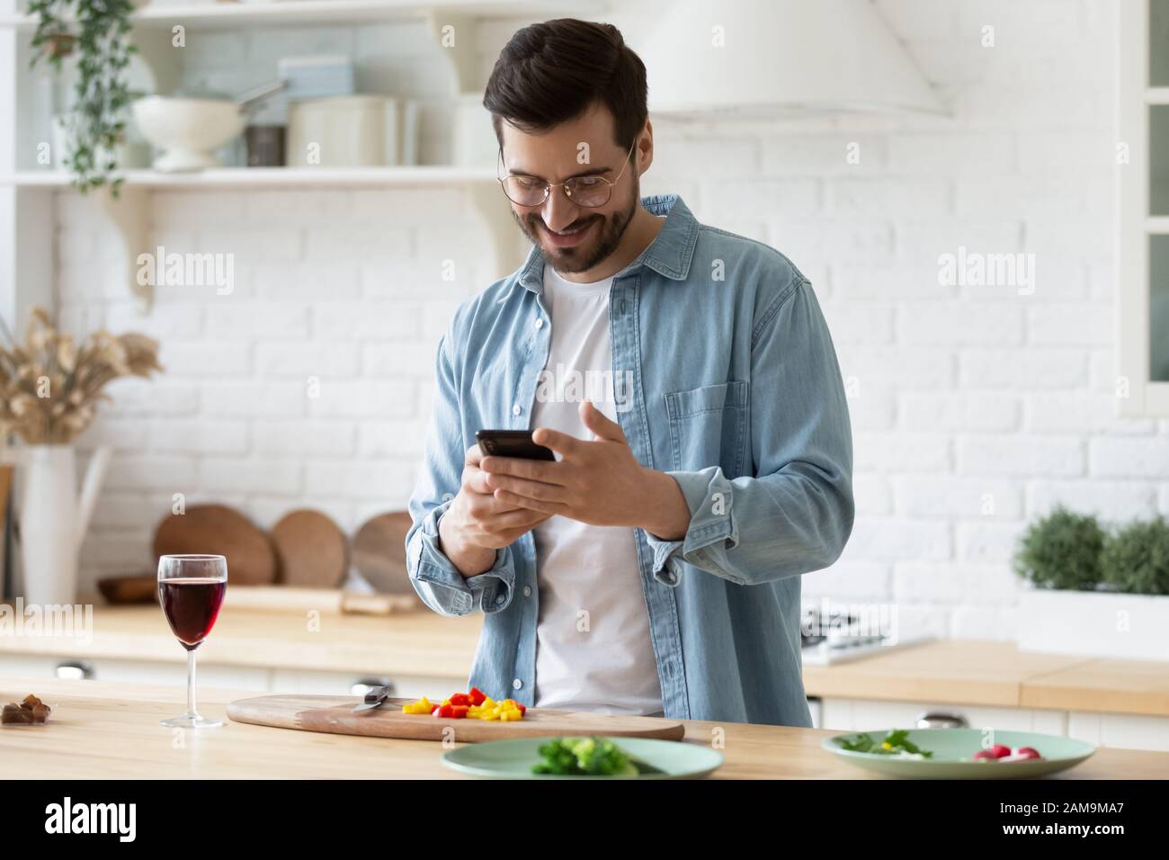 Happy millennial guy in eyeglasses web surfing recipe for meal. Stock Photo