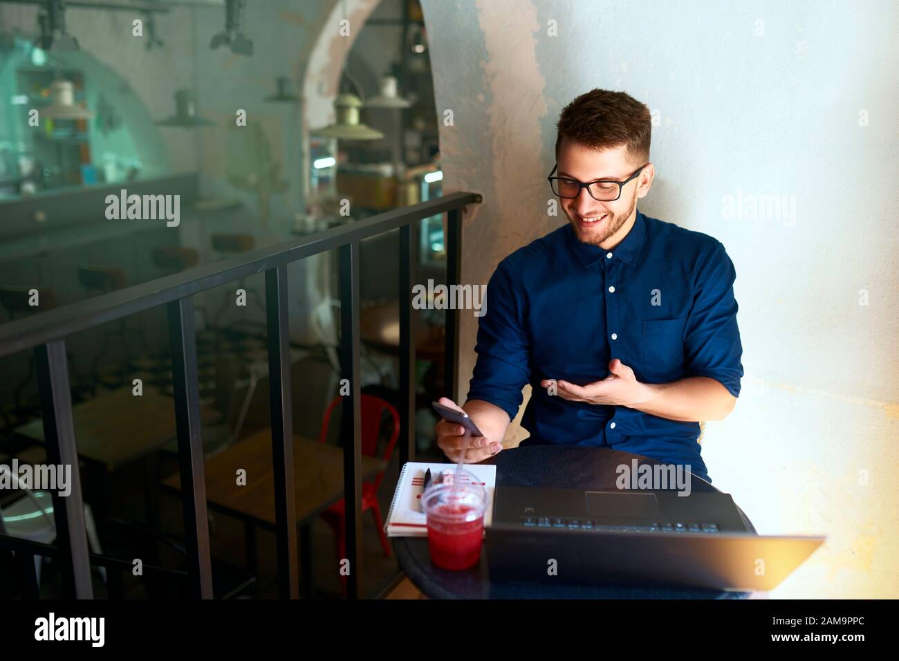 Smiling freelancer with smartphone telecommuting via online video chat. Distracted from work businessman holding mobile phone. Man in glasses with Stock Photo