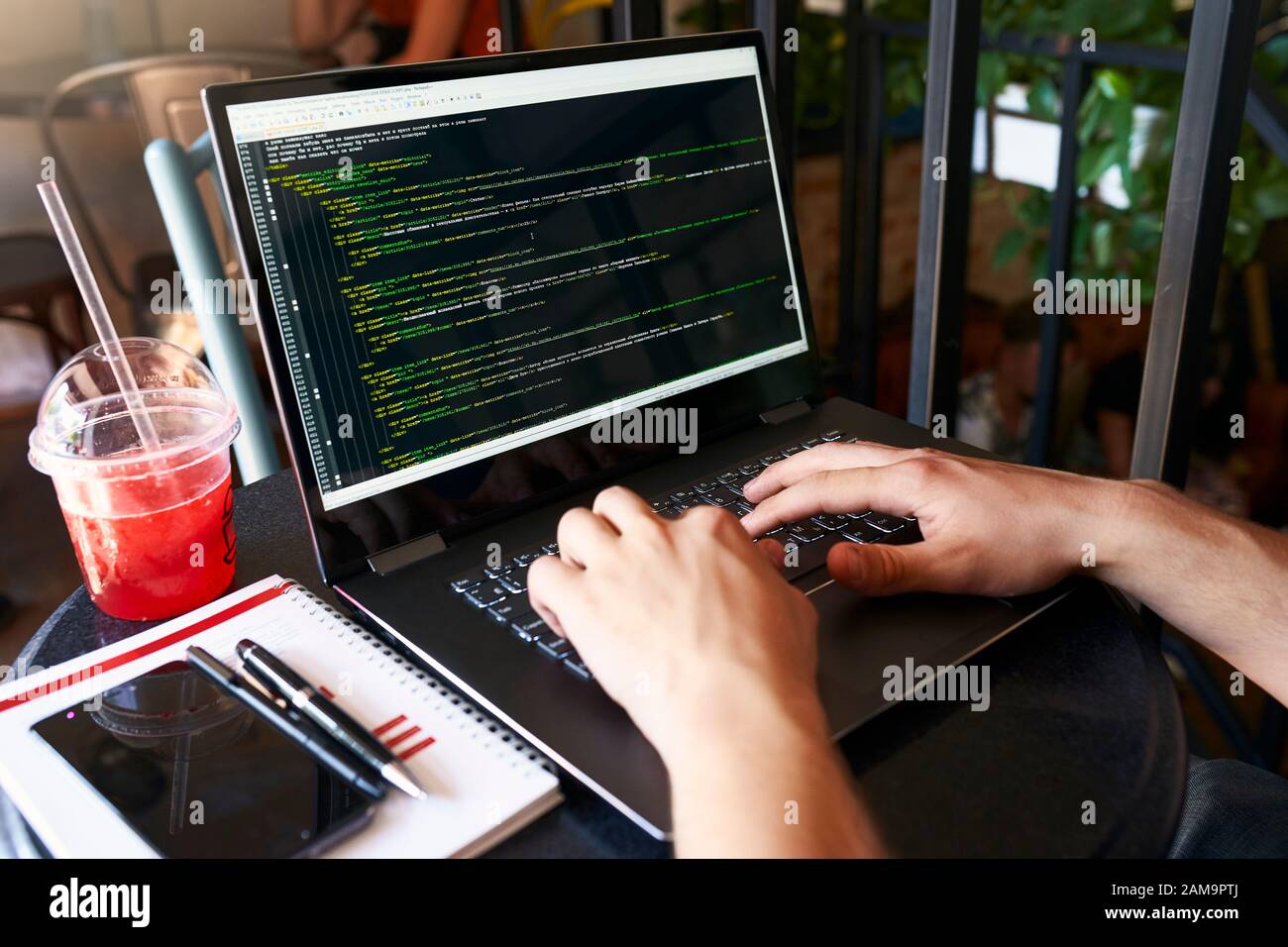 Developer programmer with laptop. Program code and script data on screen. Young freelancer in glasses working on project in cafe. Back view over the Stock Photo