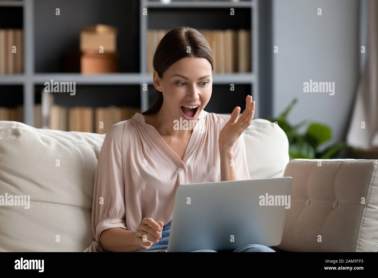 Excited millennial girl shocked by news on laptop Stock Photo