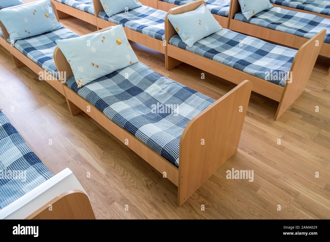 Many small beds with fresh linen in daycare preschool empty bedroom