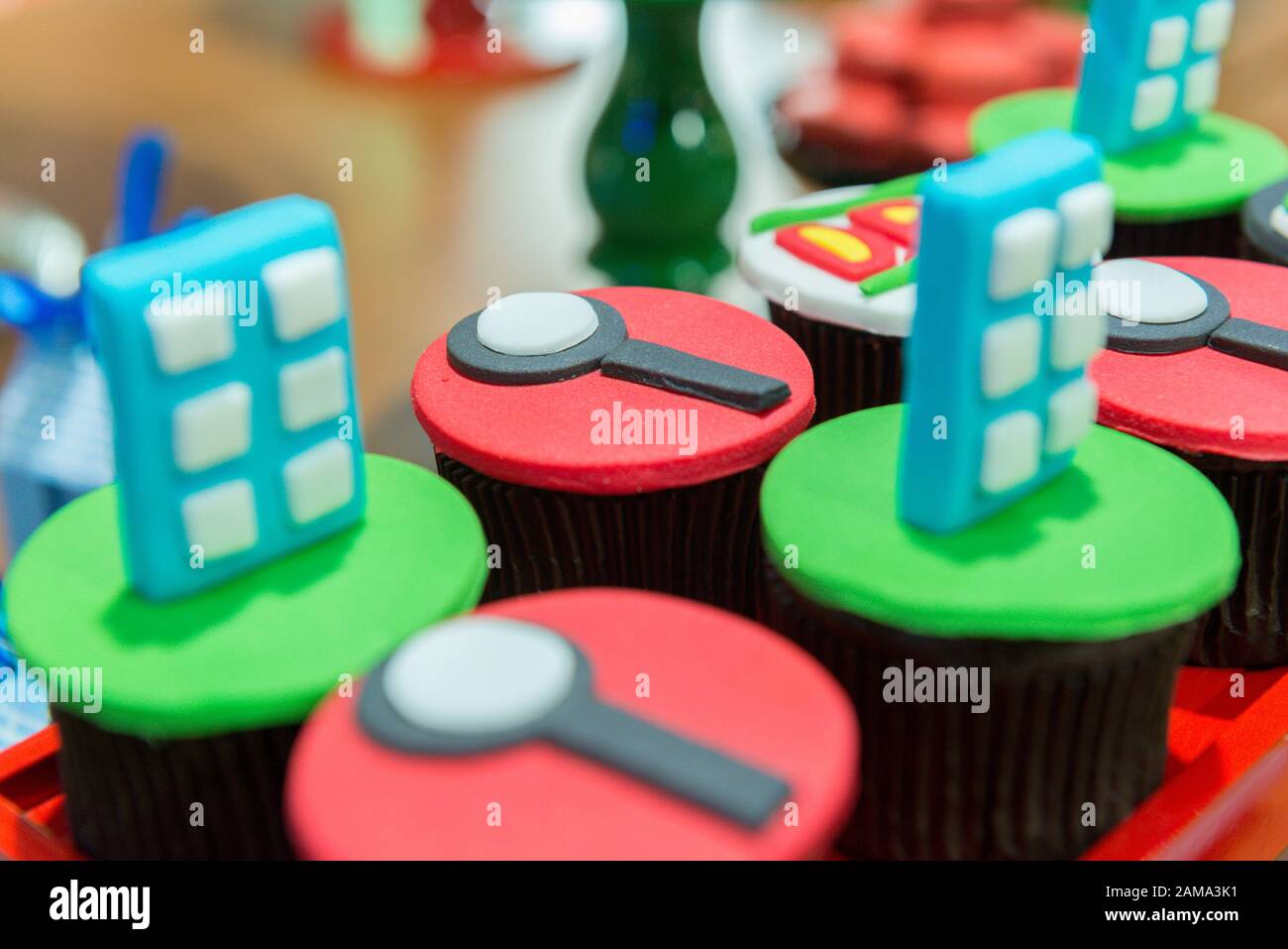 Custom cupcakes with magnifying glass fondant icing, binoculars, footprints and other conceptual research shapes on a black tray. Children's party cak Stock Photo