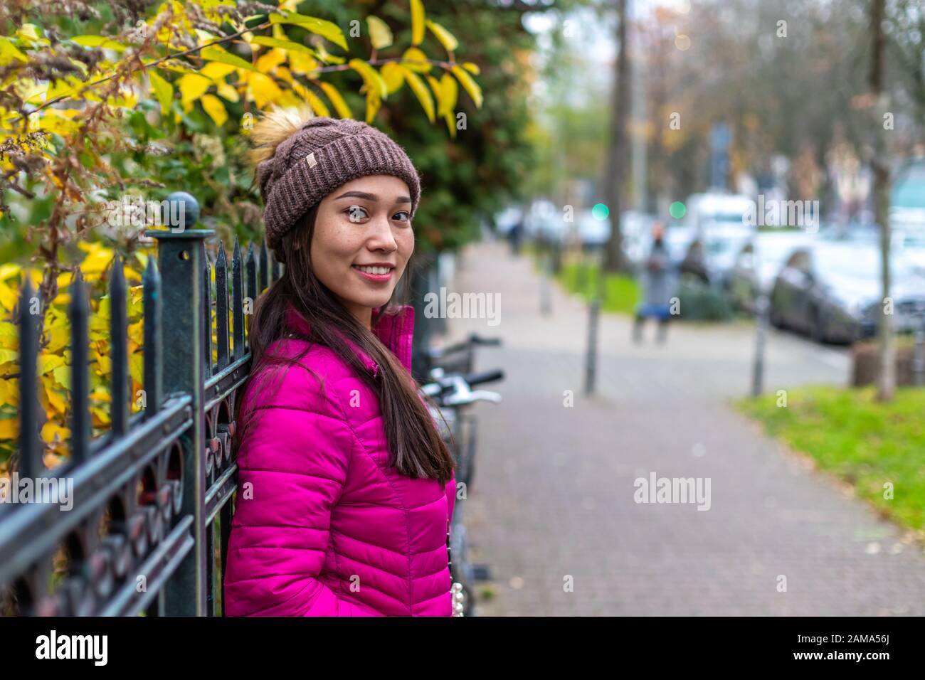 Asian girl with freckles and unusual appearance. Attractive girl in a pink jacket and Knitted hat. Blurred background with bokeh. Stock Photo