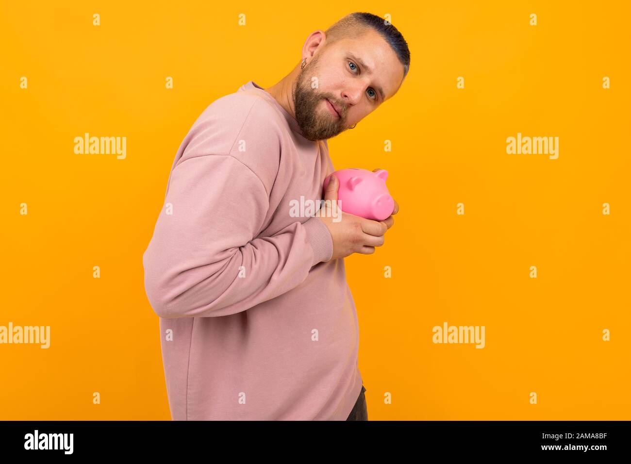 Young Strong Man With Short Black Hair Holds Pink Pig Moneybox
