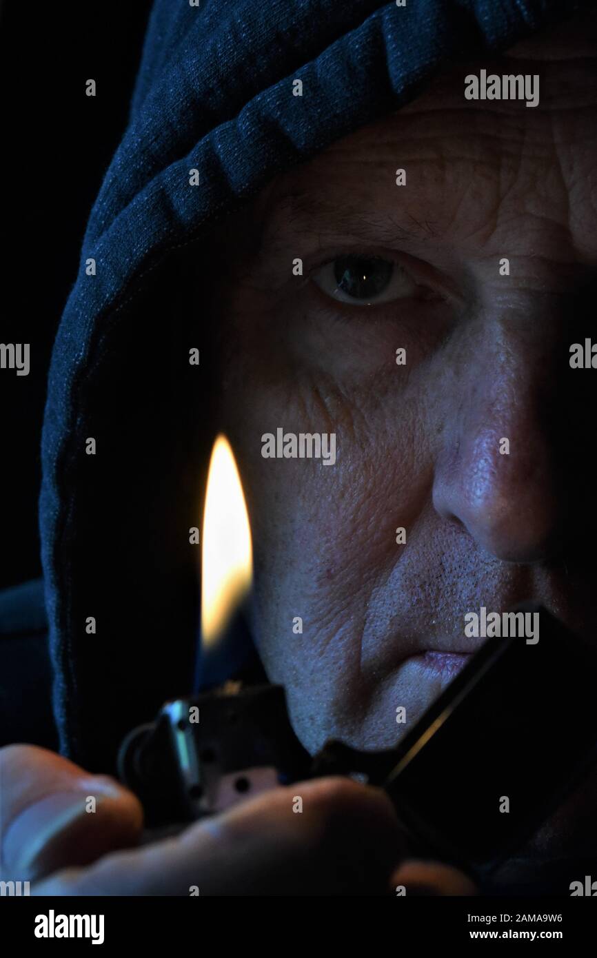 Shadowy close up of older mans face with lighter flame in the foreground Stock Photo