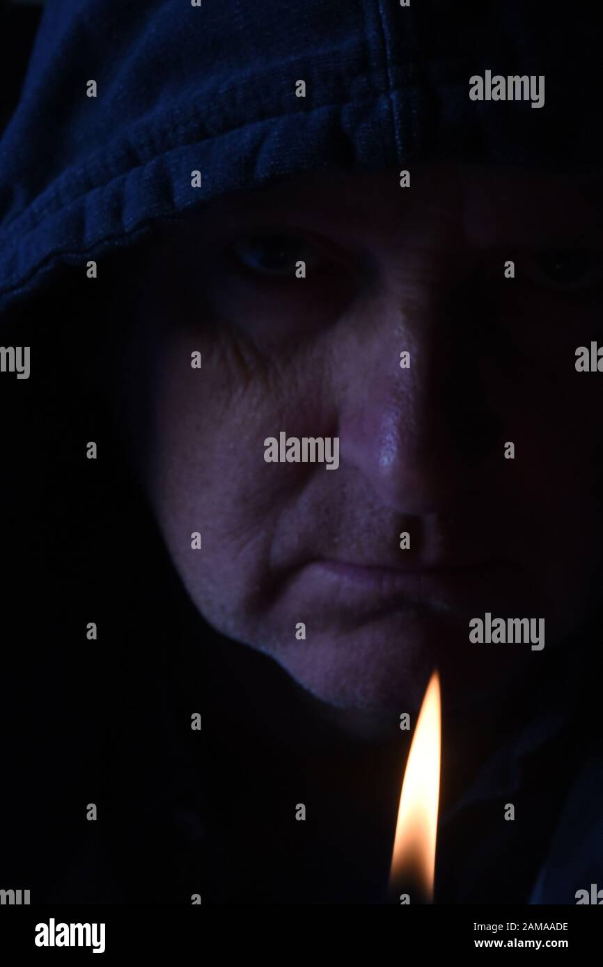 Shadowy close up of older mans face with lighter flame in the foreground Stock Photo